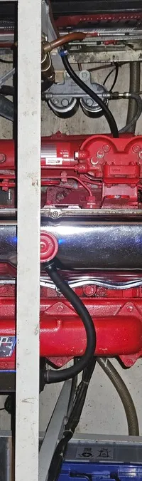 Een rode scheepsmotor met chromen kleppendeksels en de tekst "super 195" is zichtbaar in een motorruimte.