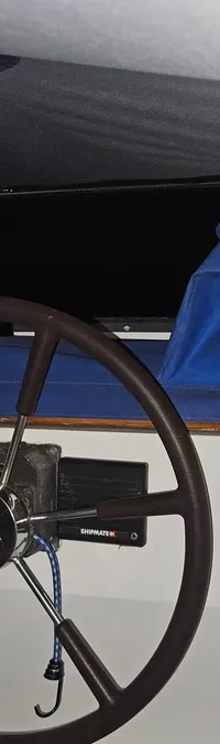 Een houten stuurwiel met een Shipmate RS-apparaat en blauwe hoezen op de banken, onder een donker plafond.