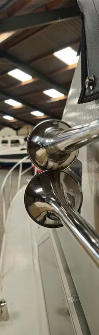 Twee glimmende, zilverkleurige scheepshoorns zijn gemonteerd op de zijkant van een witte boot in een loods. — Condor 105 Fly