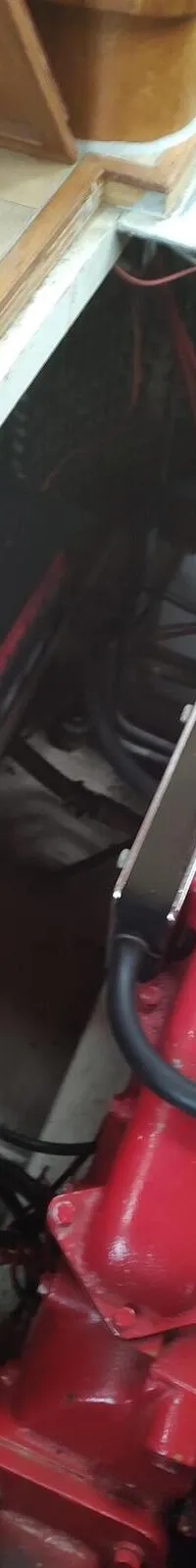 Een rode scheepsmotor met chroomkleurige onderdelen is zichtbaar, met daarnaast een zwarte accu en een tang op de vloer.