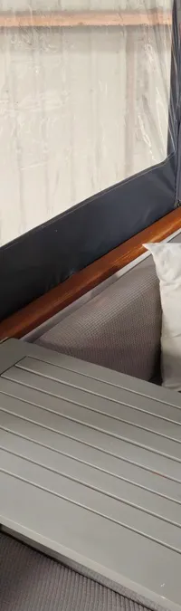 De foto toont een deel van een bootinterieur met een grijze bank, een tafel, twee kussens en een ladder.