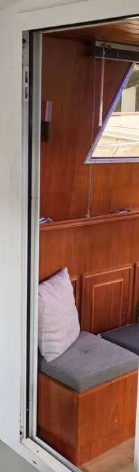 De foto toont een interieur van een boot met een houten trap, een schuifdeur en een stuurwiel zichtbaar door een raam.
