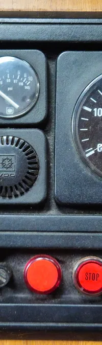 Een zwart bedieningspaneel met meters, knoppen en een contactslot, gemonteerd op een houten oppervlak.