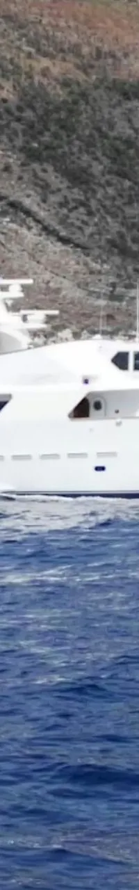 Een witte motorjacht vaart op blauw water langs een rotsachtige kustlijn onder een heldere hemel.