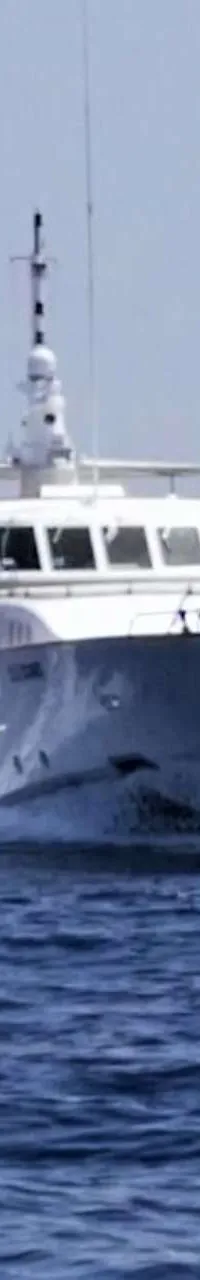 Een witte motorboot vaart over een blauwe zee, met een lichte lucht en bergen op de achtergrond. — CRN 120