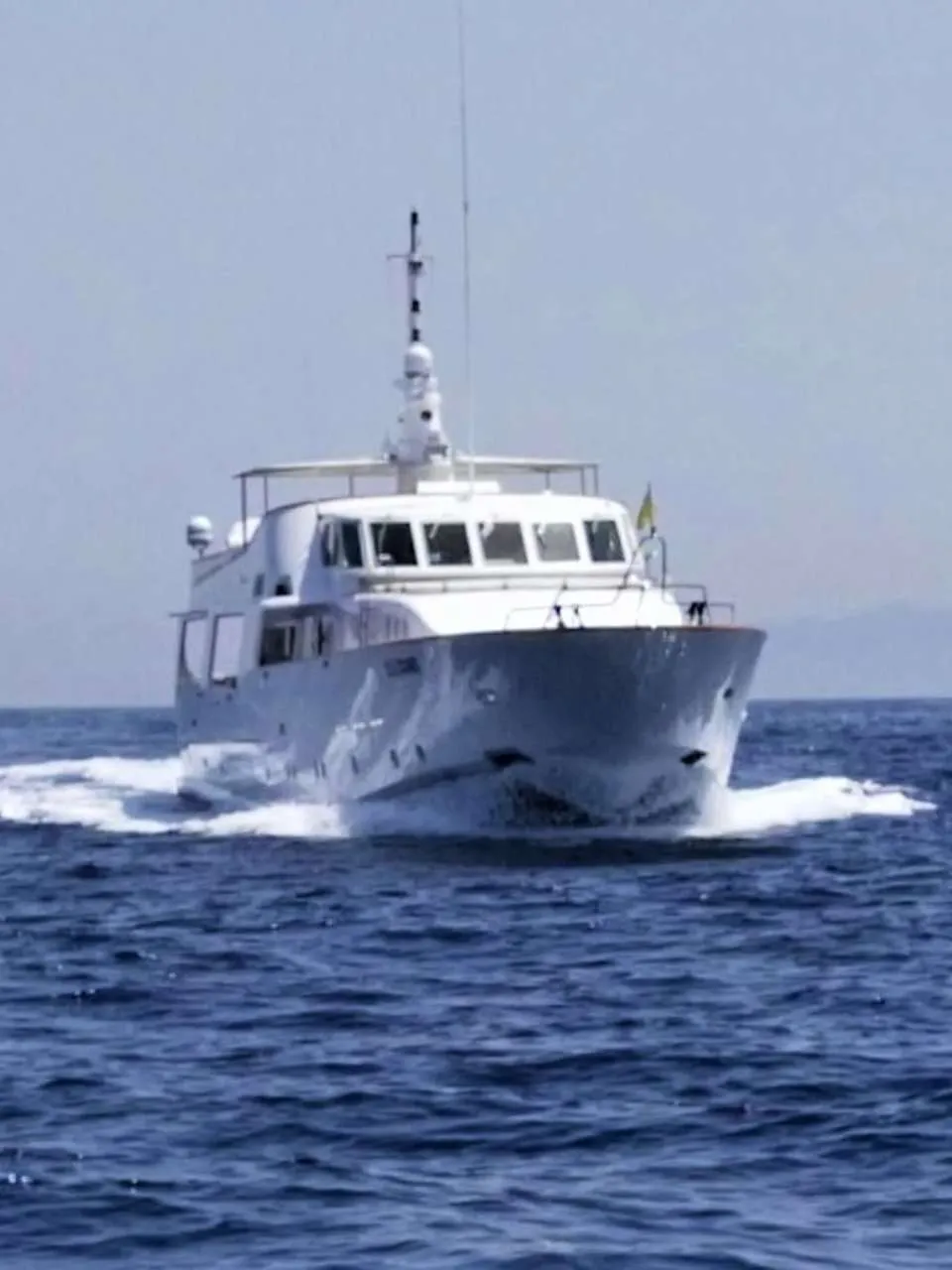 Een witte motorboot vaart over een blauwe zee, met een lichte lucht en bergen op de achtergrond. — CRN 120