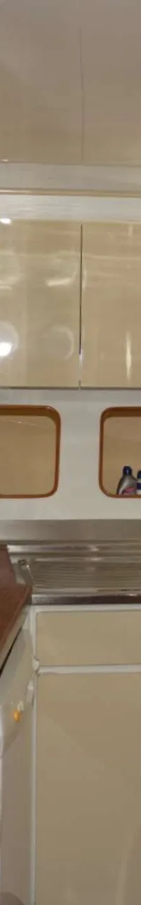 Een kombuis met een wit fornuis, afzuigkap, dubbele spoelbak, crèmekleurige kasten en patrijspoorten.