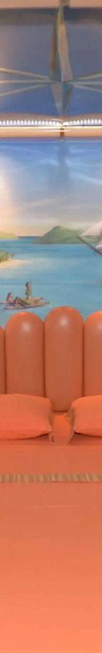 Een slaapkamer met een oranje bed, nachtkastjes en een muurschildering van een tropisch strandtafereel.