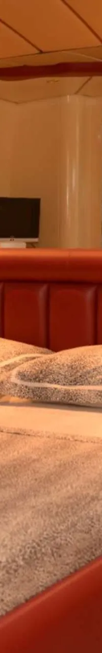 Een slaapkamer met een rood bed, twee nachtkastjes met lampen, spiegels en een televisie.