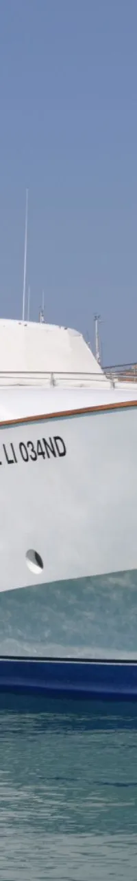 Een witte motorjacht met blauwe streep ligt aangemeerd naast een donkerblauwe boot, met "2 LI 034ND" op de boeg. — CRN 120