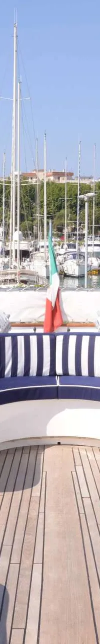 Een dek van een jacht met een blauw-wit gestreepte bank, omringd door witte hoezen en een Italiaanse vlag. — CRN 120