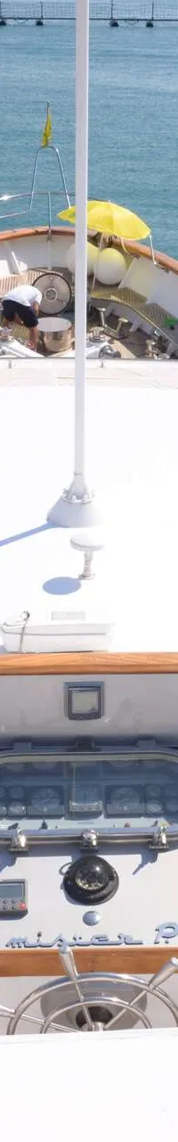 Een bovenaanzicht van een witte boot met houten details, met een stuur en bedieningspanelen, liggend in het water. — CRN 120