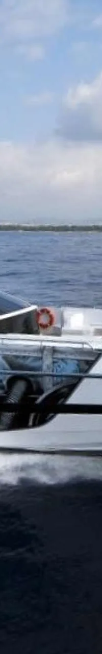 Een witte motorjacht met blauwe en zwarte accenten vaart op open water, met een kustlijn op de achtergrond.
