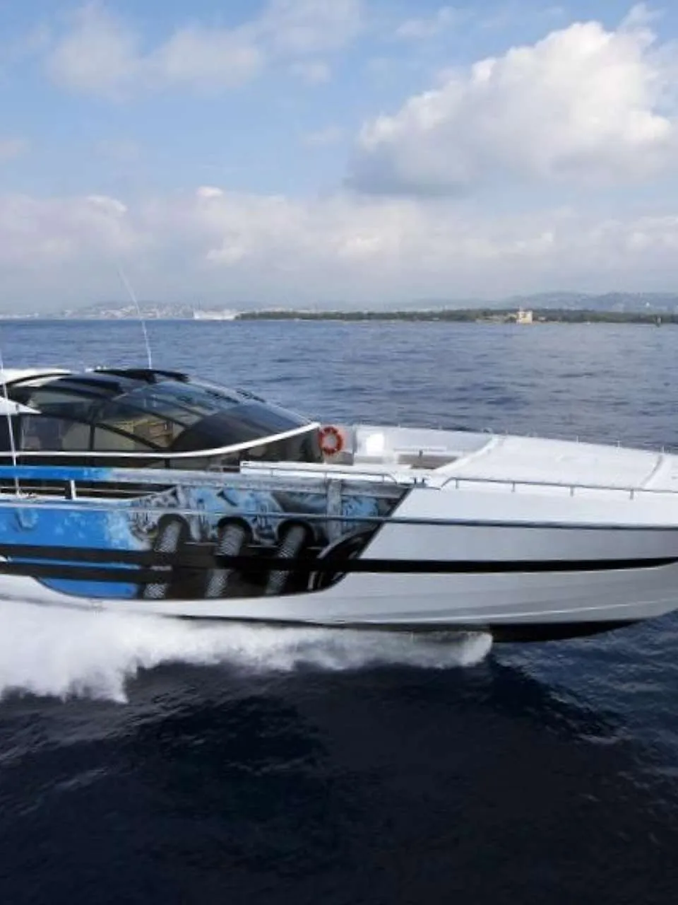 Een witte motorjacht met blauwe en zwarte accenten vaart op open water, met een kustlijn op de achtergrond.