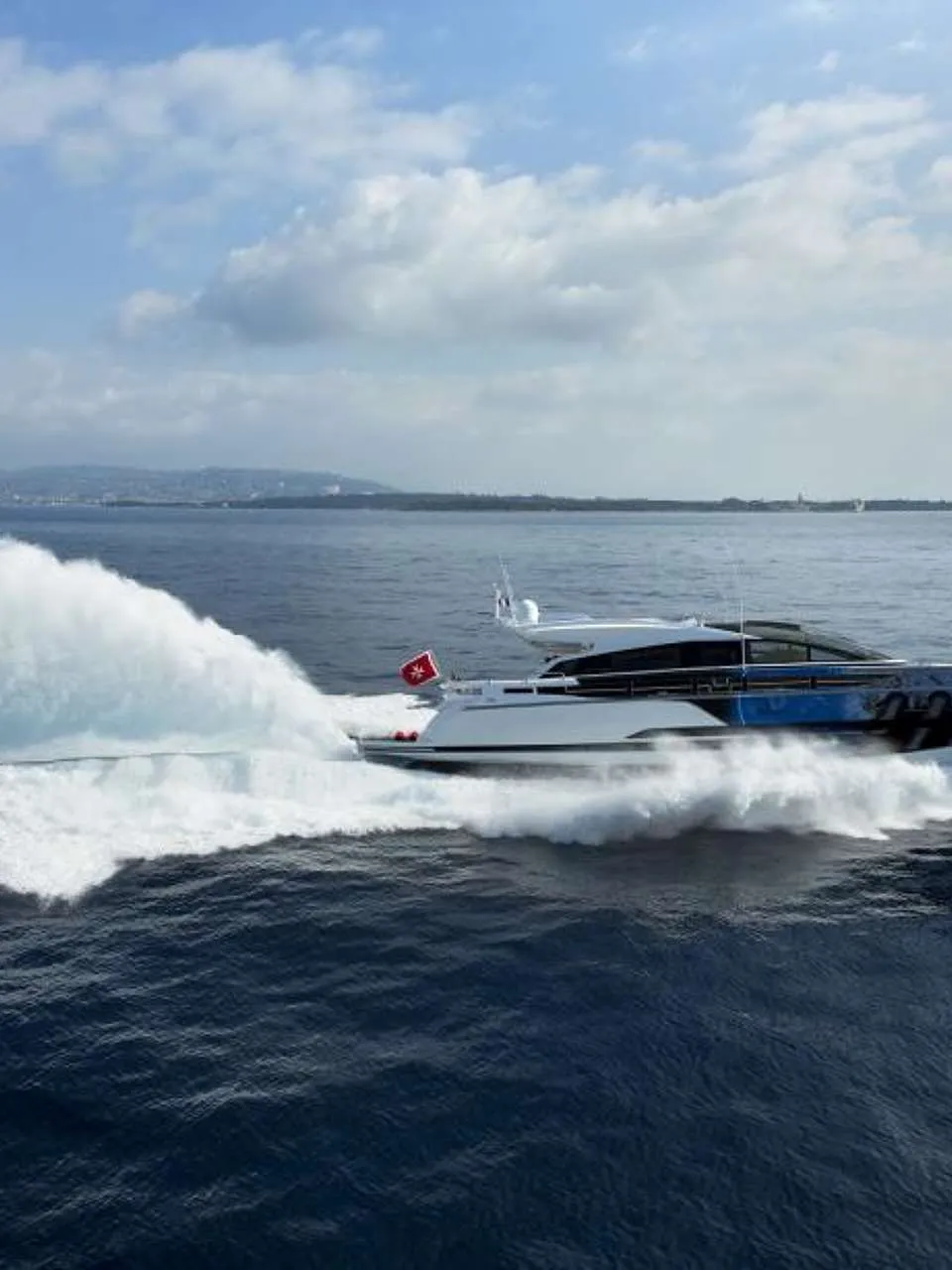 Een witte motorboot met blauwe accenten vaart snel over het water, met een grote schuimkraag achter zich. — Baia 100