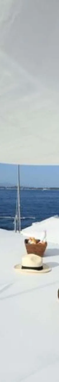 Een dek van een boot met witte kussens, handdoeken, een hoed en een mandje, onder een wit zonnescherm. — Baia 100
