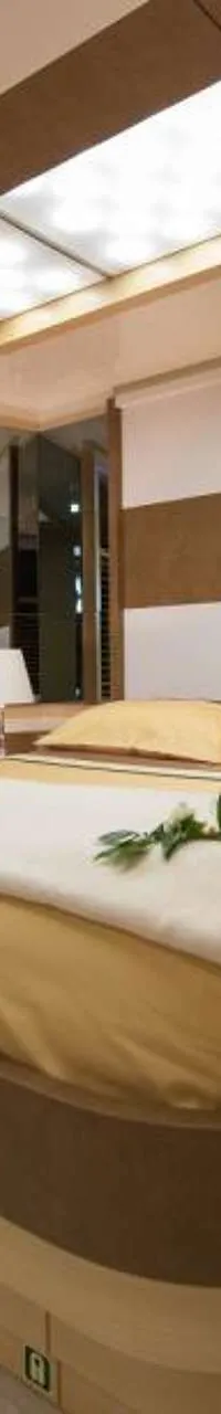 Een slaapkamer met een tweepersoonsbed, twee nachtkastjes met lampen, een stoel en ramen met jaloezieën.