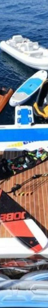 Een boot met een teakhouten dek en diverse watersportartikelen, waaronder jetski's, surfplanken en een rubberboot. — Baia 100