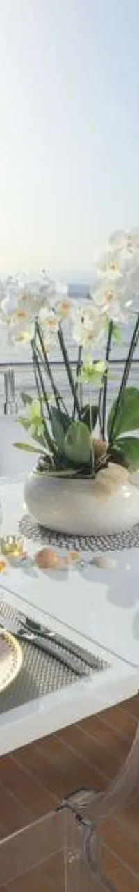 Een gedekte tafel met orchideeën en een champagnekoeler op het dek van een jacht, met de zee en kustlijn op de achtergrond.
