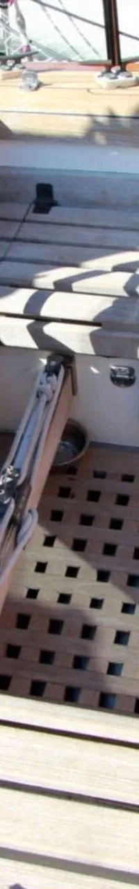 Een houten stuurwiel en een open kajuitingang met houten roosters op de vloer zijn zichtbaar op het dek van een boot.