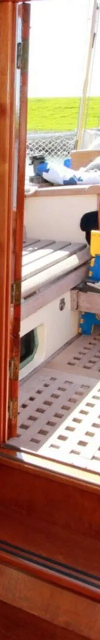 Een interieur van een boot met houten afwerking, een tafel, kussens, een brandblusser en een stuurwiel zichtbaar.