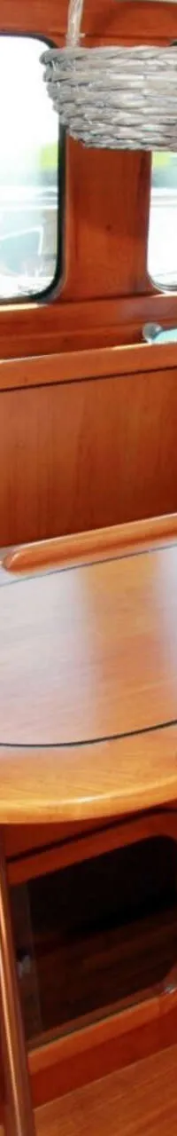 Een houten interieur met een tafel, banken met kussens, ramen en diverse scheepsbenodigdheden.