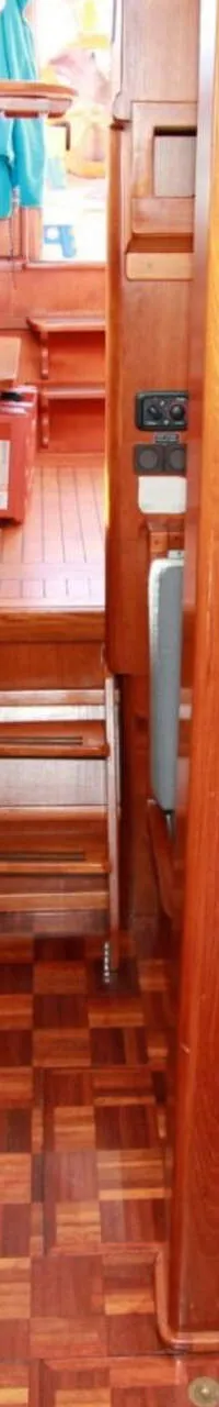 Een interieur van een boot met houten lambrisering, een zithoek met tafel, een kombuis en een trap naar een hoger dek.