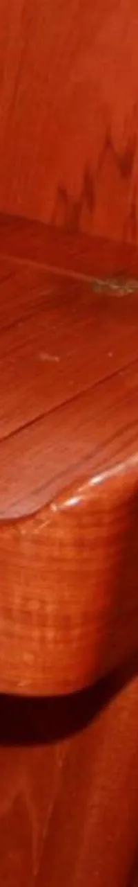 Een houten kajuitinterieur met een bureau en kastjes, met een wit snoer en een grijs kussen zichtbaar.