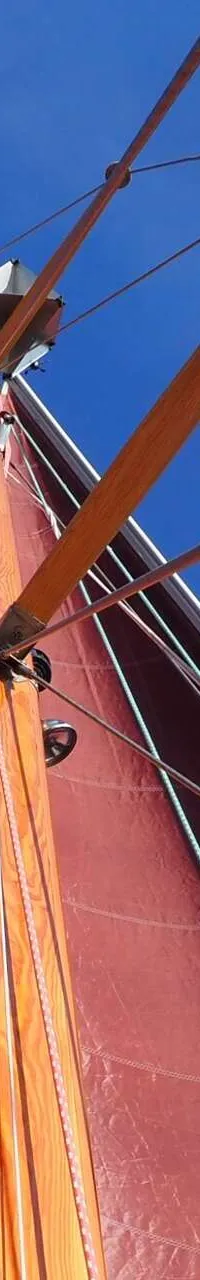 Een rode zeilboot met een houten mast en giek, gezien vanuit een laag perspectief tegen een helderblauwe lucht. — Volkerak 46