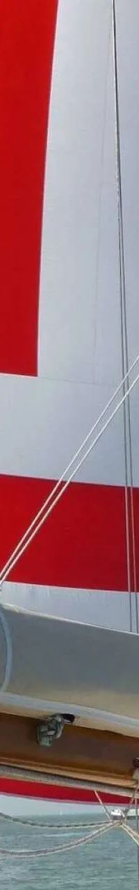 Een rood-wit gestreept zeil is deels opgerold en deels uitgerold, met een mast en giek zichtbaar.