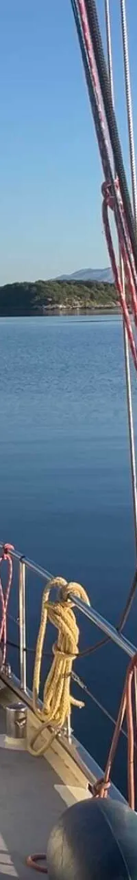 Een zeilboot met een houten kajuit en zonnepanelen op het dak vaart op rustig water met eilanden en bergen op de achtergrond.