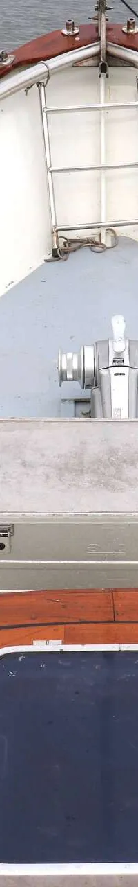De boeg van een boot is zichtbaar met een houten dek, luik, aluminium kist, ankerlier, touwen en reling.