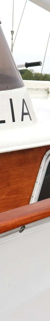 Een witte boot met houten accenten en de naam "CECILIA" op de zijkant, ligt aangemeerd met stootwillen.