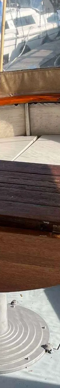 Een houten klaptafel met een metalen voet staat in een boot met een rondlopende bank en ramen. — Bloemsma Kotter 10.50