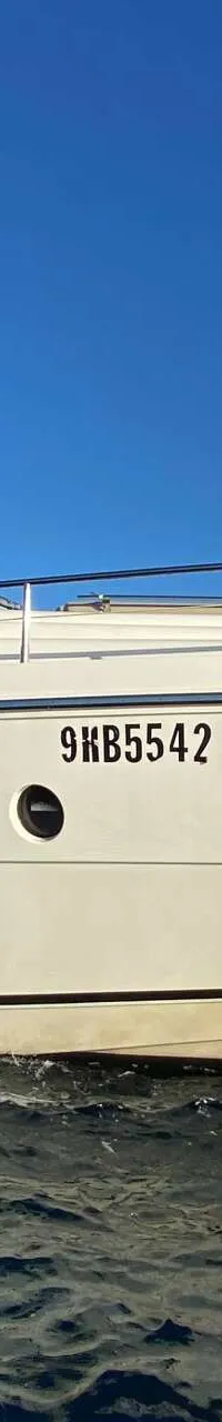 Een witte motorjacht met registratienummer 9KB5542 vaart op blauw water onder een heldere blauwe lucht.
