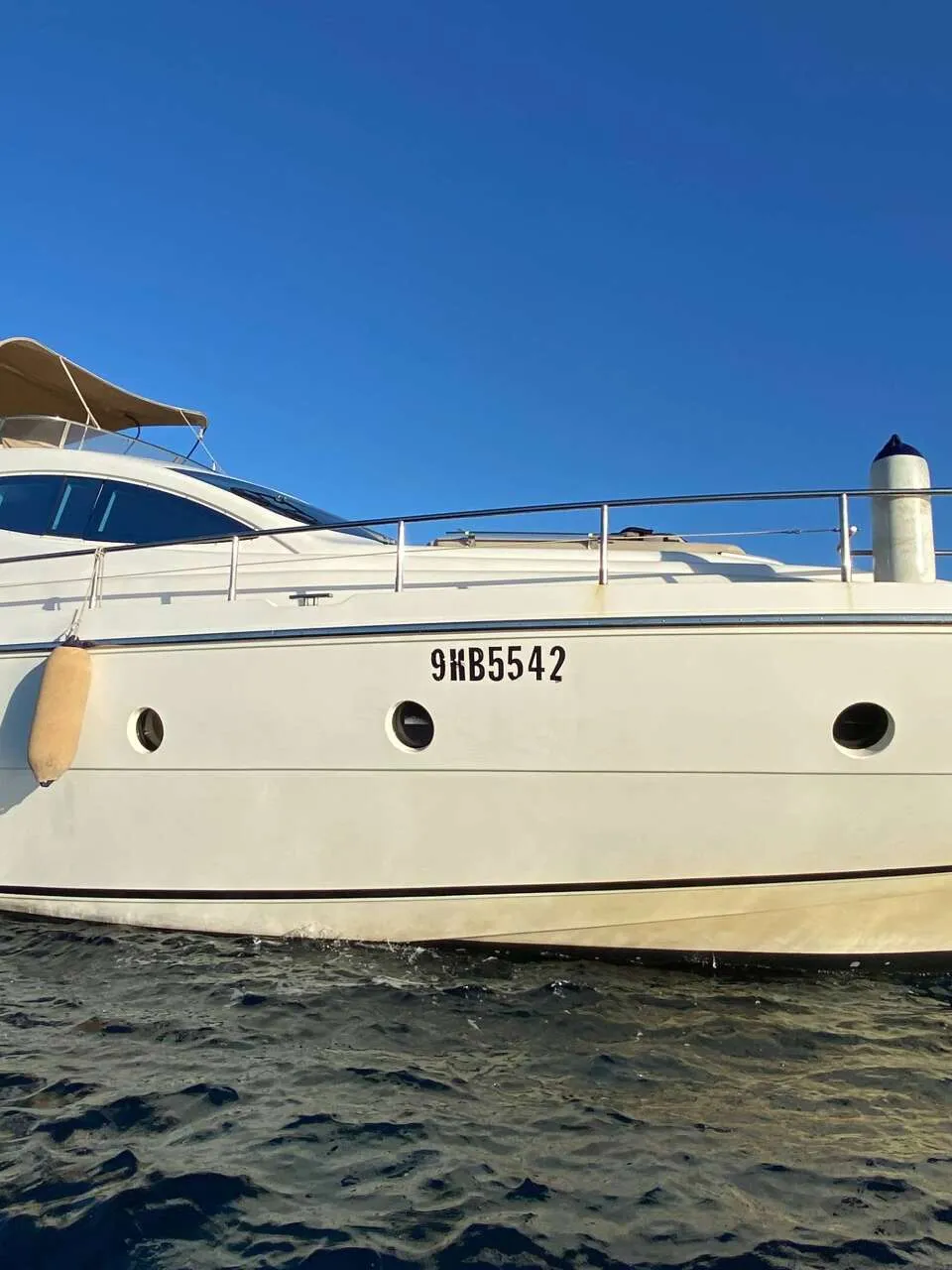 Een witte motorjacht met registratienummer 9KB5542 vaart op blauw water onder een heldere blauwe lucht.