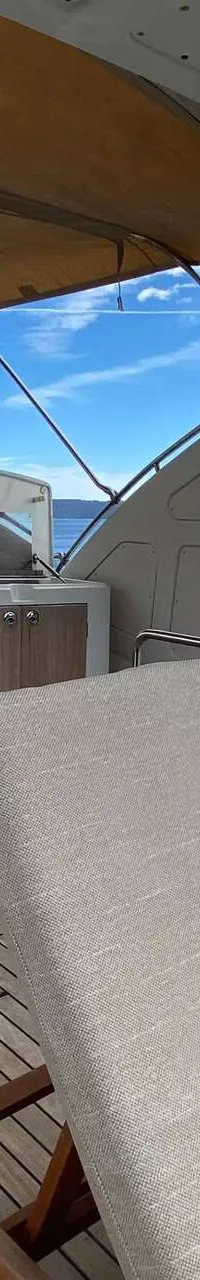 Een dek van een jacht met teakhouten vloer, ligstoelen, een tafel met bloemen en een buitenkeuken, met uitzicht op zee.