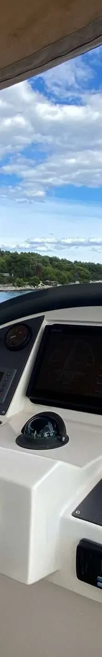 De foto toont het stuur van een boot met een dashboard vol meters, een kompas en een scherm, met een waterlandschap op de…