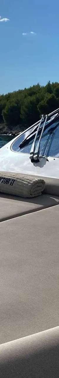 Een boot met een zonnedek en twee opgerolde handdoeken met de tekst "PHILIP VICTOR II" erop, met de zee en een beboste…
