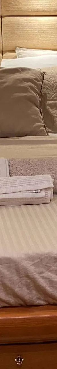 Een bed met beige beddengoed en kussens, met opgerolde handdoeken, in een kajuit met houten wanden. — Aicon 64