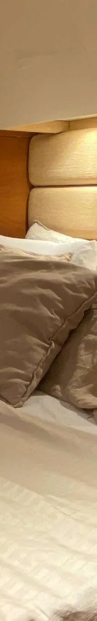Een slaapkamer met een tweepersoonsbed, twee leeslampjes, een raam met rolgordijn en houten wandpanelen.