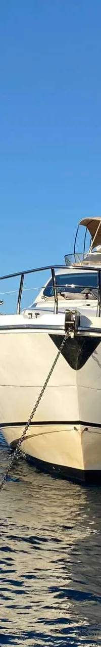 Een witte motorboot ligt voor anker in blauw water, met een rotsachtige kustlijn op de achtergrond. — Aicon 64