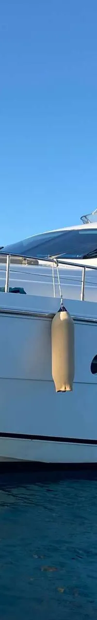 Een witte motorjacht met een beige zonnescherm en stootwillen drijft op blauw water onder een heldere hemel.