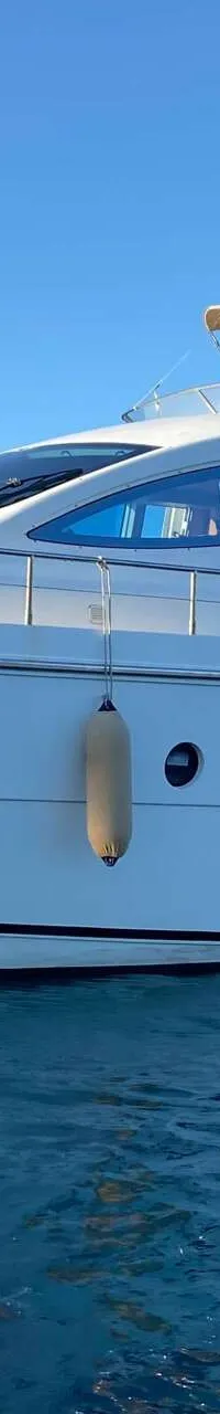 Een witte motorjacht met blauwe ramen en een beige zonnescherm ligt in helderblauw water onder een strakblauwe lucht.