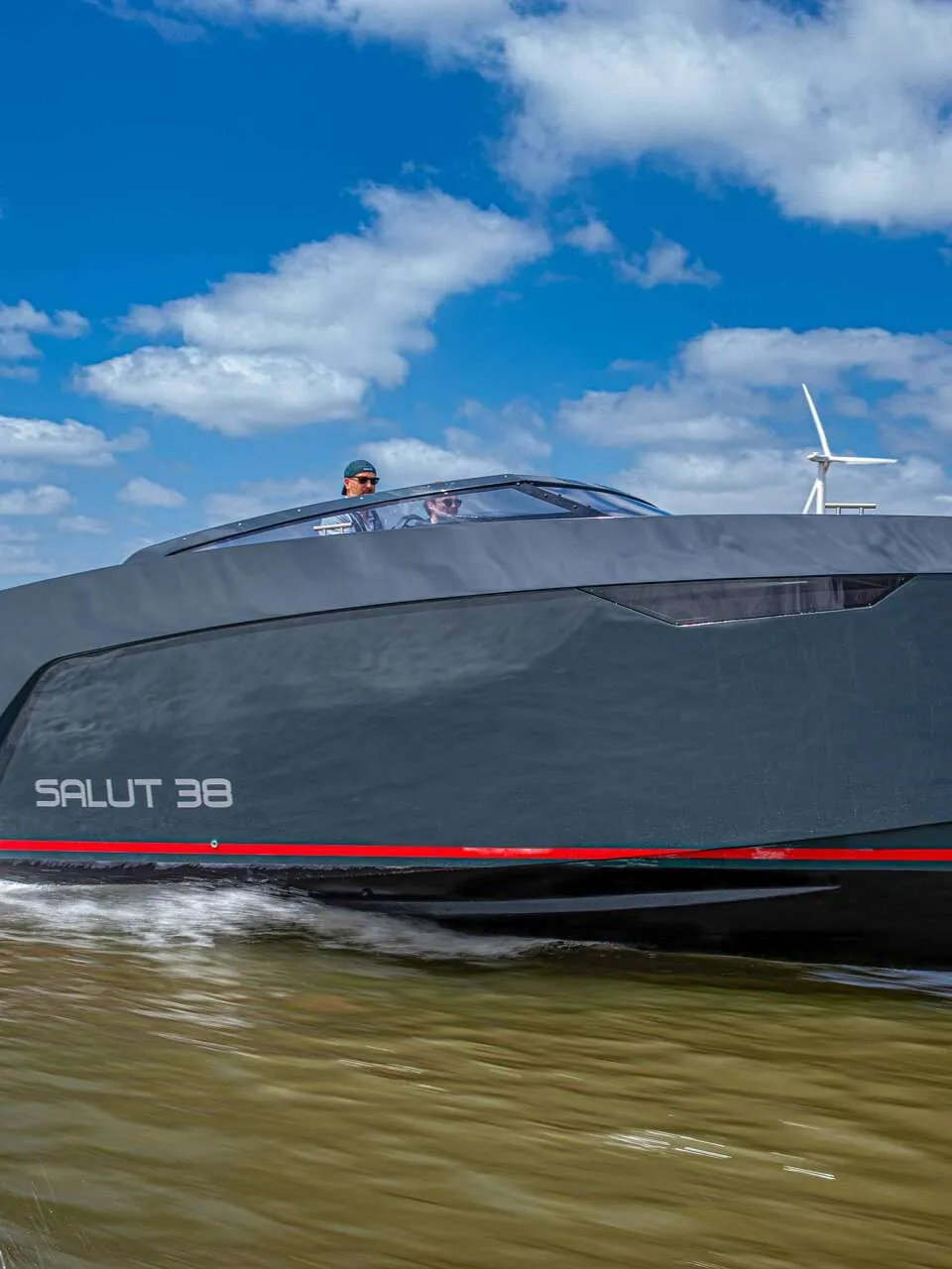 Een donkergrijze motorboot met de tekst "SALUT 38" en een rode streep op de zijkant vaart over water. — Salut 38