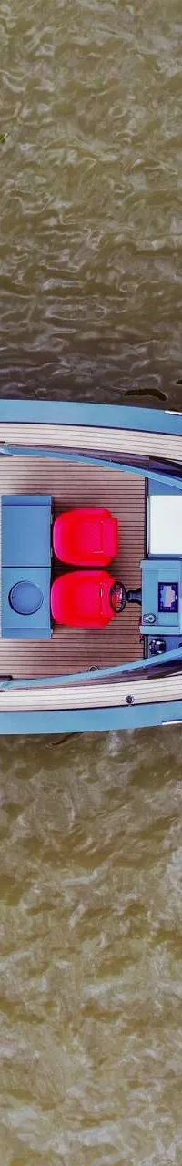 Een blauwe boot met een houten dek, twee rode stoelen en een rood zonnedek, drijvend op bruin water. — Salut 38