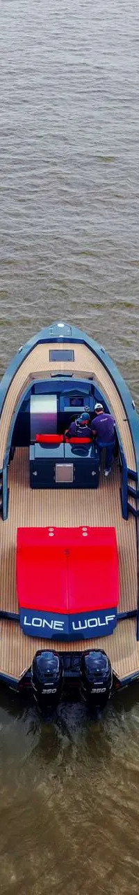 Een blauwe boot met houten dek en rode accenten, genaamd "LONE WOLF", ligt in het water. — Salut 38