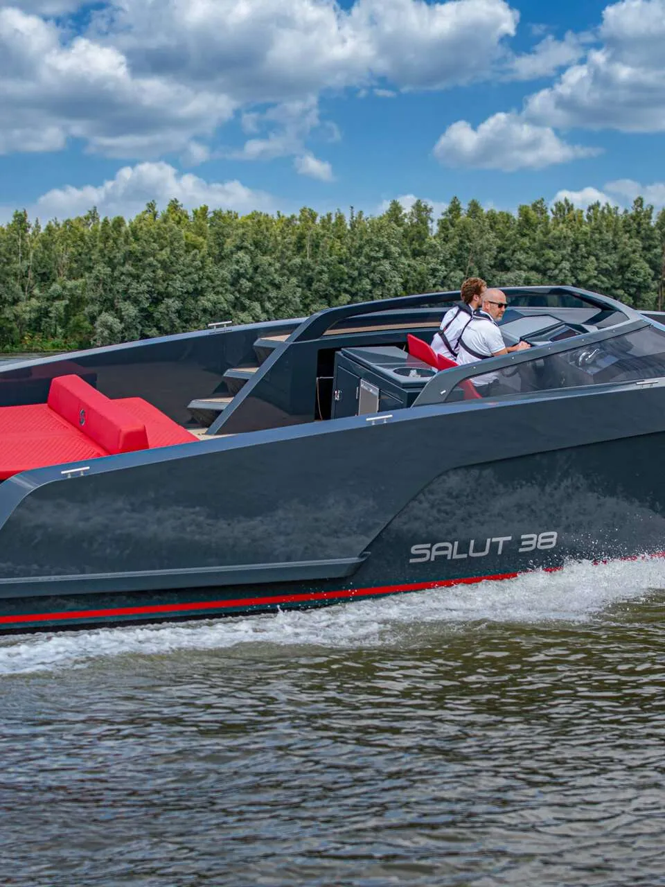 Een donkergrijze motorboot met rode accenten en twee buitenboordmotoren vaart op het water met twee personen aan boord.