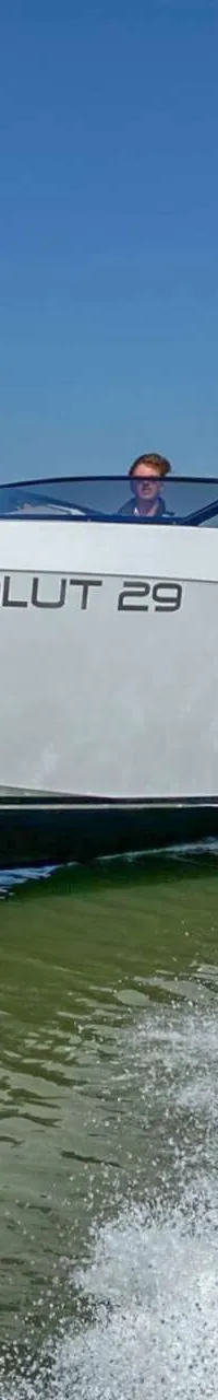 Een witte motorboot met de naam "SALUT 29" vaart op open water, met twee personen aan boord en een duidelijke boeggolf.