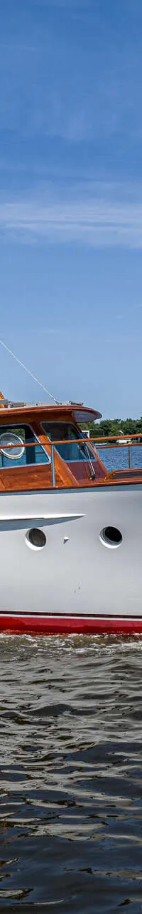 Een witte motorboot met houten opbouw en een rode streep op de romp vaart over water onder een blauwe lucht.